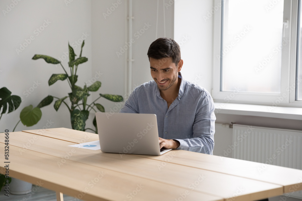 Man office employee work on laptop sit at desk in cozy workplace use corporate program looks satisfied by work results, e-mailing to client, search helpful information on internet. Modern tech concept Man office employee work on laptop sit at desk in cozy workplace use corporate program looks satisfied by work results, e-mailing to client, search helpful information on internet. Modern tech concept