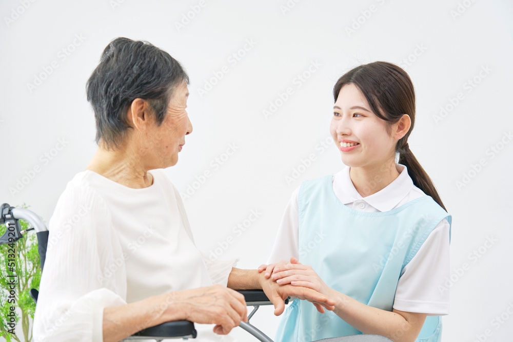 室内で車椅子に乗る高齢者女性と会話する介護士 室内で車椅子に乗る高齢者女性と会話する介護士