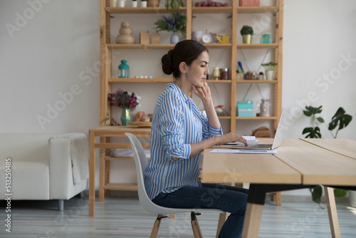 Businesswoman sit at desk text e-mail use laptop, busy in freelance, looks focused, thinking, solve business distantly, makes research, working on-line. Modern tech usage, connection, workflow concept