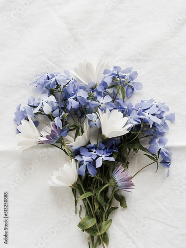 Flowers background. White and blue summer flowers bouquet on white linen texture background top view Poster