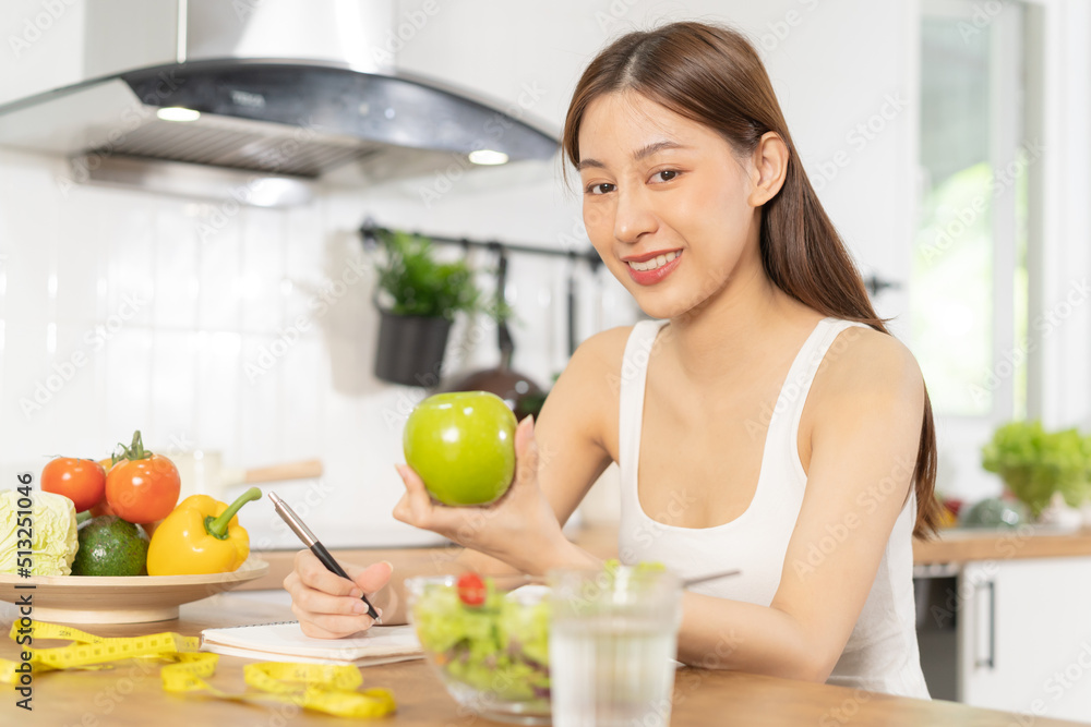 Diet, Dieting asian young woman working, write diet plan right nutrition, hold green apple, vegetables salad is food for good health not choose eat junk food. Nutritionist female, Weight loss person.
