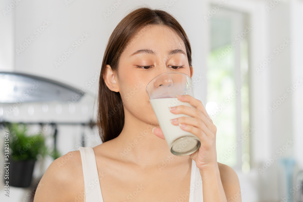 Happy, Asian young woman, girl drinking a glass of white fresh, warm or hot dairy milk for calcium, vitamin wholesome good nutrition in morning at kitchen home. lifestyle, product healthy people.