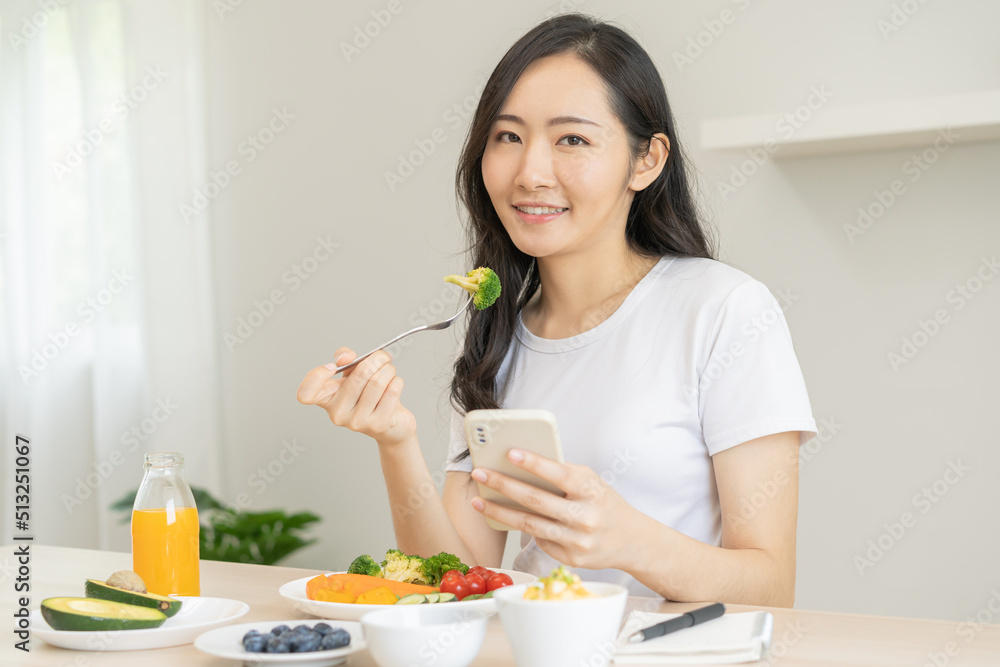 Dieting, asian young woman eating, holding fork at broccoli, diet plan nutrition with fresh vegetables salad, enjoy meal while using smartphone. Nutritionist of healthy, nutrition of weight loss. Dieting, asian young woman eating, holding fork at broccoli, diet plan nutrition with fresh vegetables salad, enjoy meal while using smartphone. Nutritionist of healthy, nutrition of weight loss.