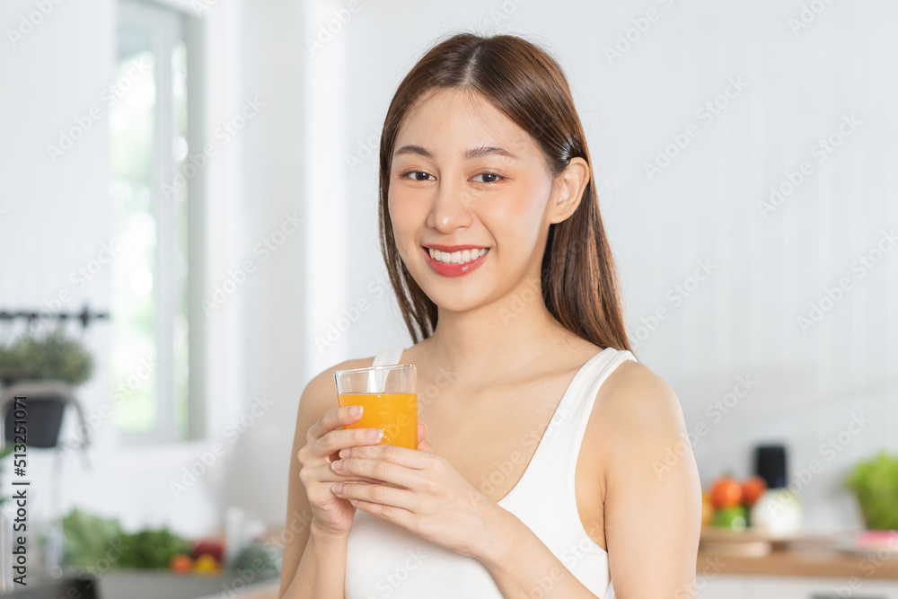 Happy housewife, smile asian young woman, girl drinking fresh orange juice in a glass drink in the kitchen, holding transparent glass in her hand, thirsty at home. Health care, healthy diet concept. Happy housewife, smile asian young woman, girl drinking fresh orange juice in a glass drink in the kitchen, holding transparent glass in her hand, thirsty at home. Health care, healthy diet concept.