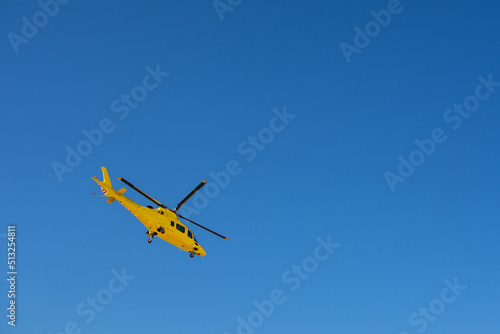 Yellow rescue helicopter taking flight on a blue background. Image with copy space