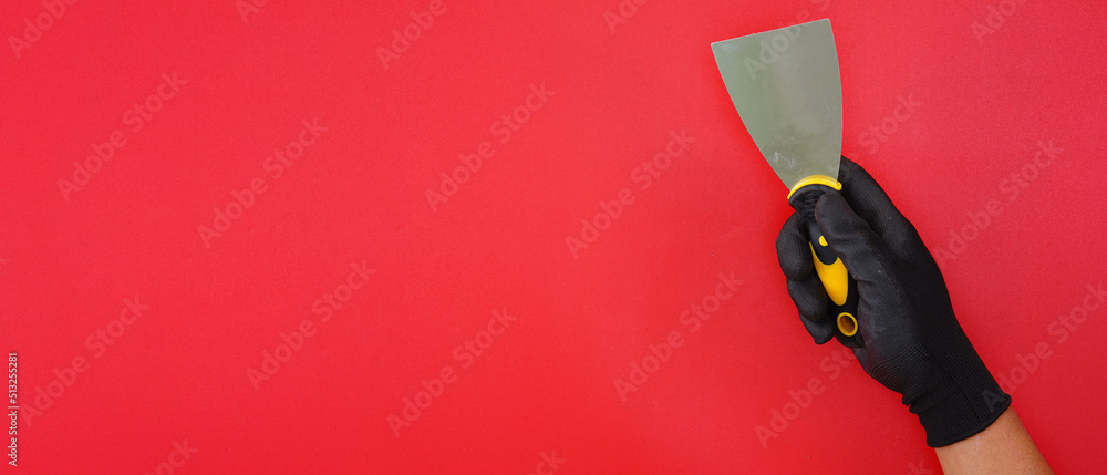 hand wearing black gloves holding putty knife scraper isolated red background - obrazy, fototapety, plakaty 