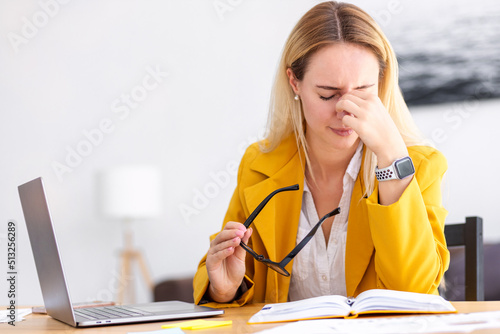 Tired stressed caucasian woman having headache feeling sick, pain, depression, overwork concept. Female rubs the bridge of his nose, holding eyeglasses photo