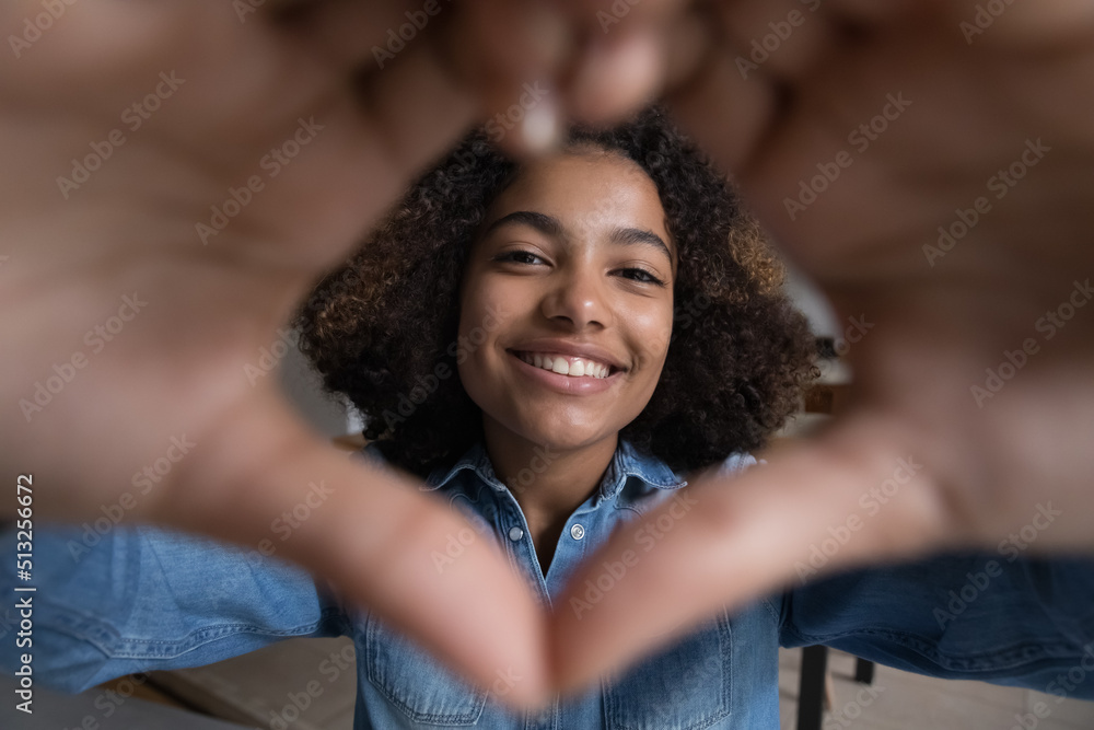 Beautiful African teenage girl make heart symbol with joined fingers in front of camera, close up cropped view face through affection sign. I Love You declaration, sincere feelings, first love concept Beautiful African teenage girl make heart symbol with joined fingers in front of camera, close up cropped view face through affection sign. I Love You declaration, sincere feelings, first love concept