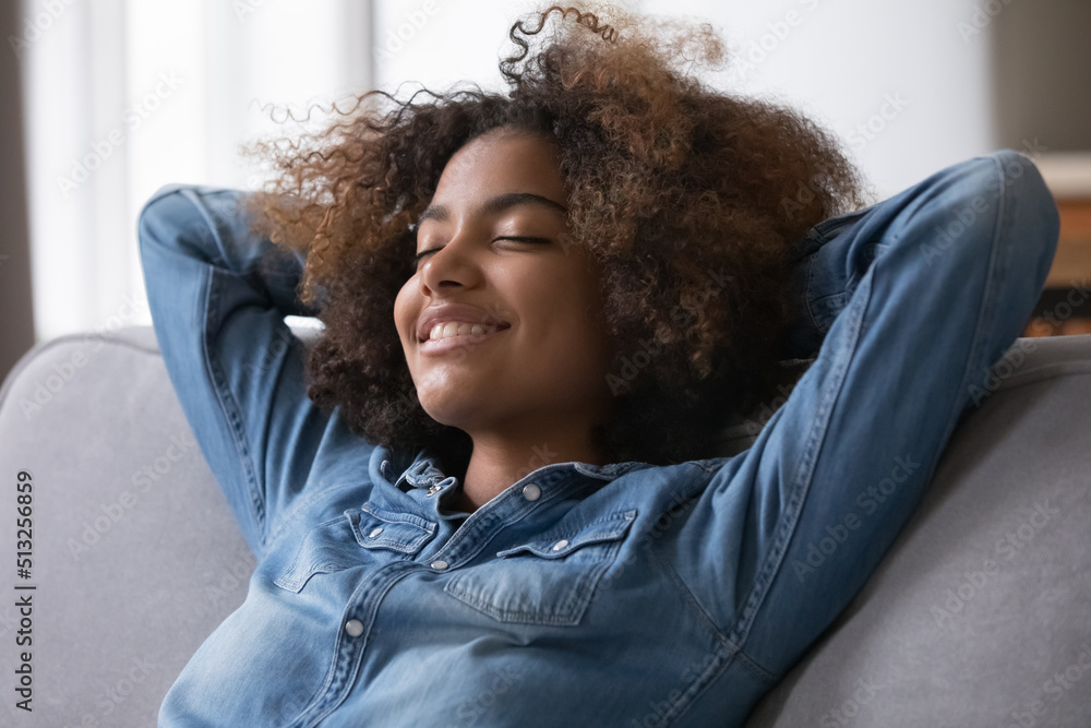 Fototapeta premium Close up beautiful peaceful African teenage girl relaxing alone at modern home breathing fresh conditioned air in cozy warm living room. Enjoy stress free weekend, repose, healthy daytime nap concept