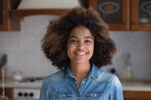 Head shot beautiful African teenage girl posing alone in domestic kitchen at home smile look at camera, having wide toothy charming smile and natural curly hairs. Beauty, gen Z person portrait concept