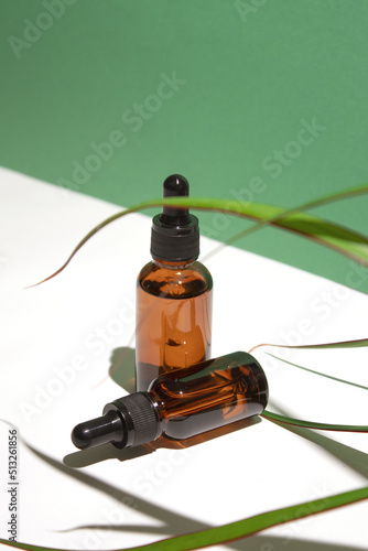 Amber glass dropper bottles different sizes with leaves on white green background. Hyaluronic acid oil, serum with collagen and peptides skin care product.