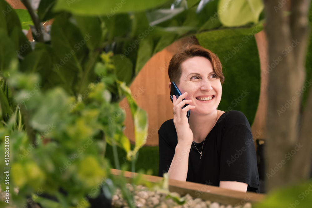 Attractive young woman with a short haircut sits at a table in a cafe and talks on the phone. Woman smiles during a telephone conversation. Attractive young woman with a short haircut sits at a table in a cafe and talks on the phone. Woman smiles during a telephone conversation.