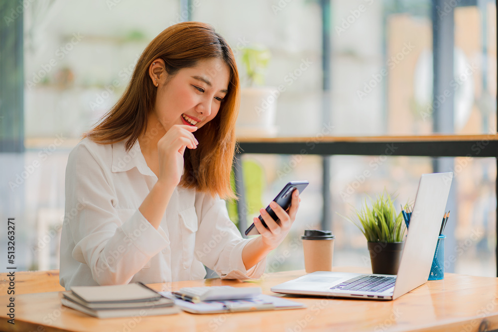 Portrait of Asian businesswoman sitting at a desk and working on a laptop computer with a phone call and financial graph documents on the table. Portrait of Asian businesswoman sitting at a desk and working on a laptop computer with a phone call and financial graph documents on the table.