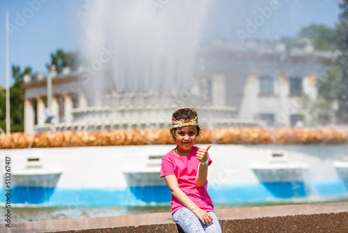 Loving life. Cheerful little girl having fun and posing near blue fountain water. Summer vacation. Happy child in summer hot day.