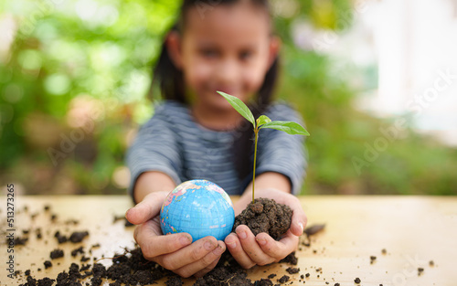 Blurred of little girl is holding plant and globe model together, concept of ESG, environment, earth day, sustainability, world environment day, montessori education for kid and home school.