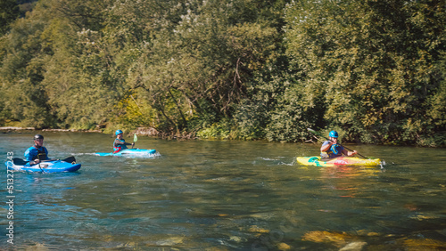 Three kayakers paddling and maneuvering on the fast-moving river with a rocky shore and going under the concrete bridge