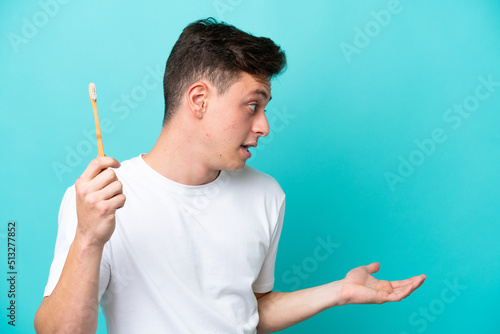 Young Brazilian man brushing teeth isolated on blue background with surprise expression while looking side