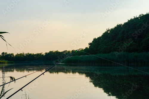 Fishing adventures, carp fishing. A fisherman is fishing at sunset. Fishing rods on the river bank. Landscape. © Dmitry