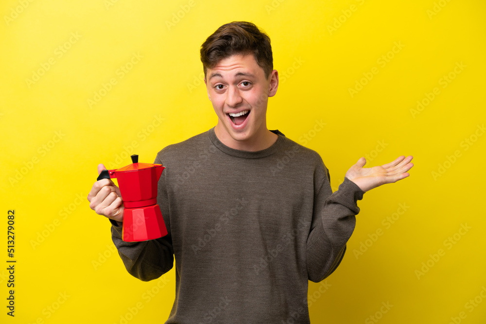 Young Brazilian man holding coffee pot isolated on yellow background with shocked facial expression Young Brazilian man holding coffee pot isolated on yellow background with shocked facial expression