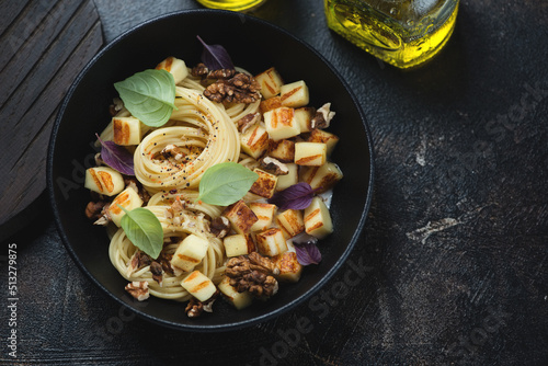 Black bowl with haloumi cheese and walnuts spaghetti, high angle view on a dark-brown stone background, studio shot