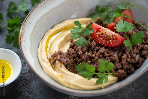 Closeup of hummus served with ground beef meat and fresh parsley in a grey bowl, selective focus
