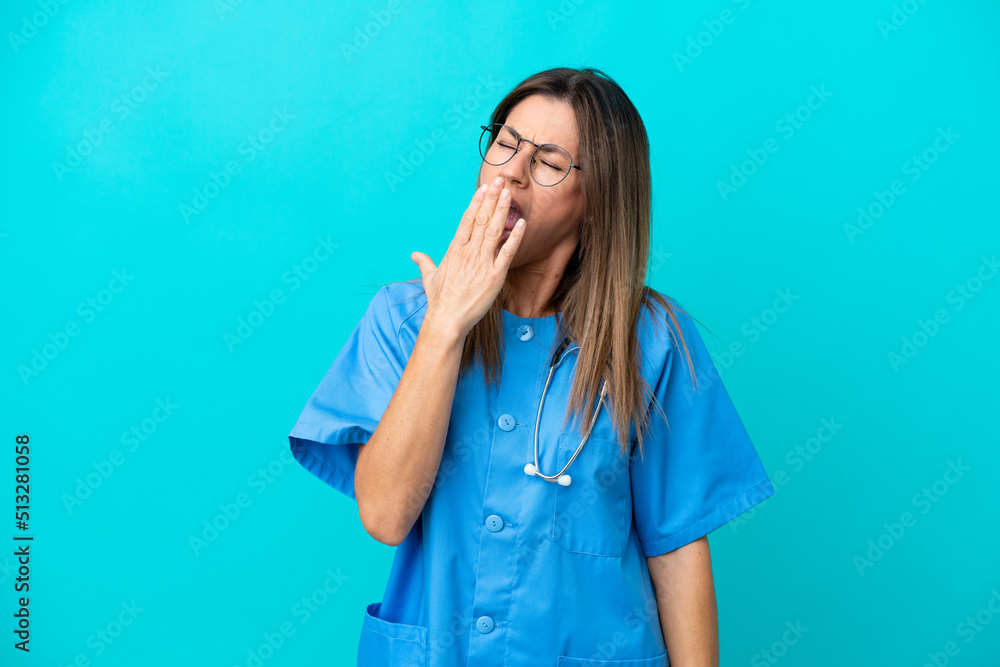 Middle age surgeon woman isolated on blue background yawning and covering wide open mouth with hand Middle age surgeon woman isolated on blue background yawning and covering wide open mouth with hand
