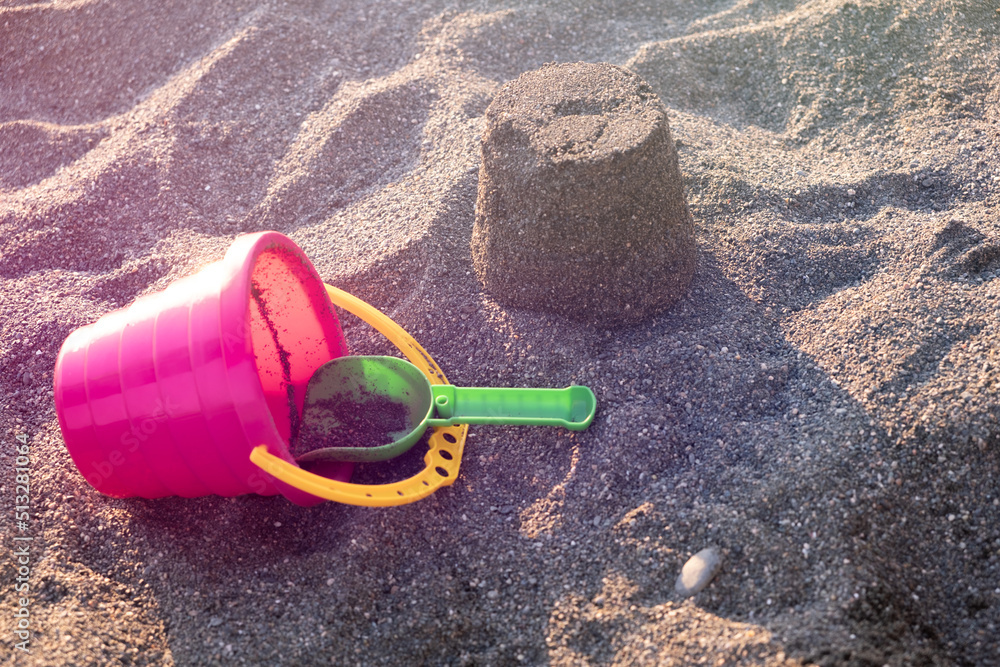 Red bucket, green rake on the beach sand on a sunny summer day Red bucket, green rake on the beach sand on a sunny summer day