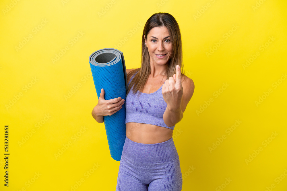 Sport woman going to yoga classes while holding a mat isolated non yellow background doing coming gesture Sport woman going to yoga classes while holding a mat isolated non yellow background doing coming gesture