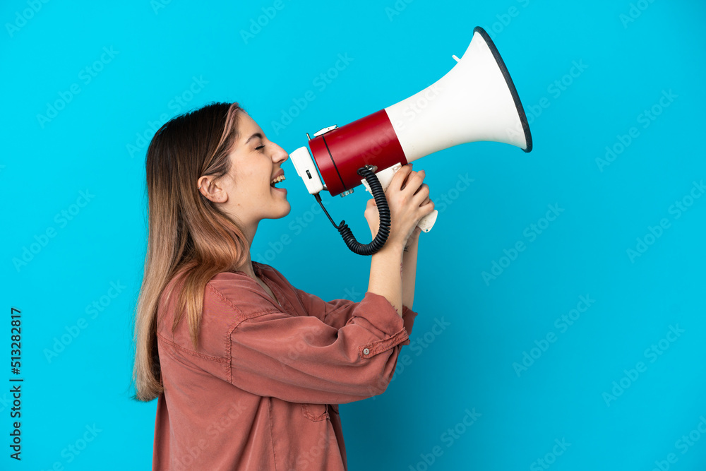 Young caucasian woman isolated on blue background shouting through a megaphone to announce something in lateral position Young caucasian woman isolated on blue background shouting through a megaphone to announce something in lateral position