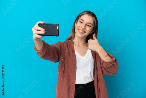 Young caucasian woman isolated on blue background making a selfie with mobile phone