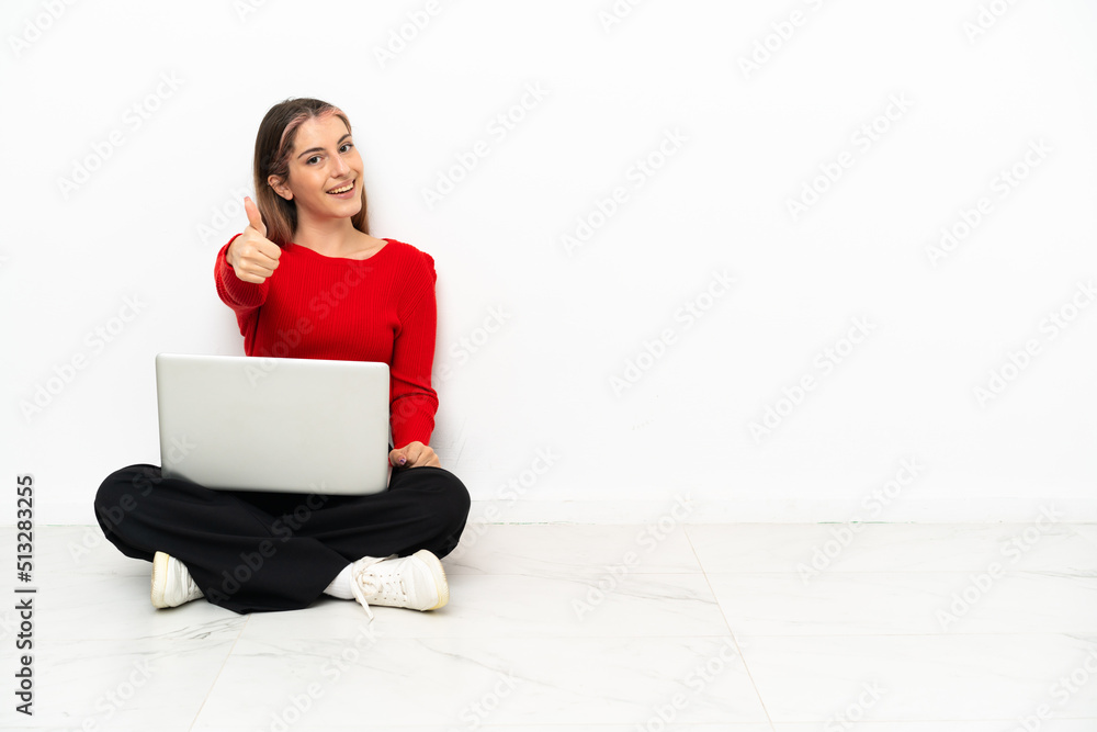 Young caucasian woman with a laptop sitting on the floor with thumbs up because something good has happened Young caucasian woman with a laptop sitting on the floor with thumbs up because something good has happened