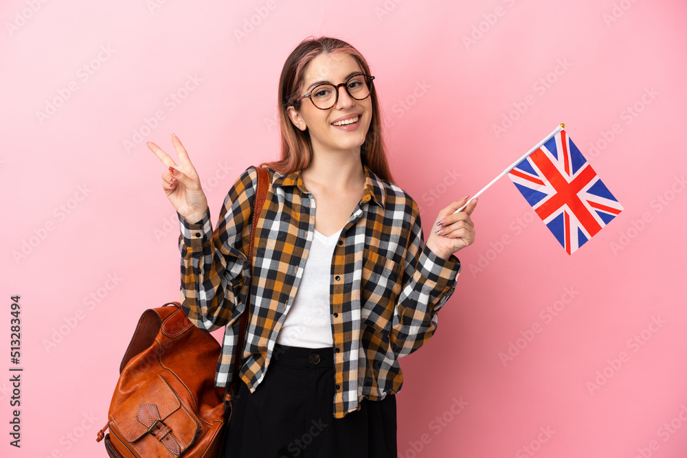Young hispanic woman holding an United Kingdom flag isolated on pink background smiling and showing victory sign