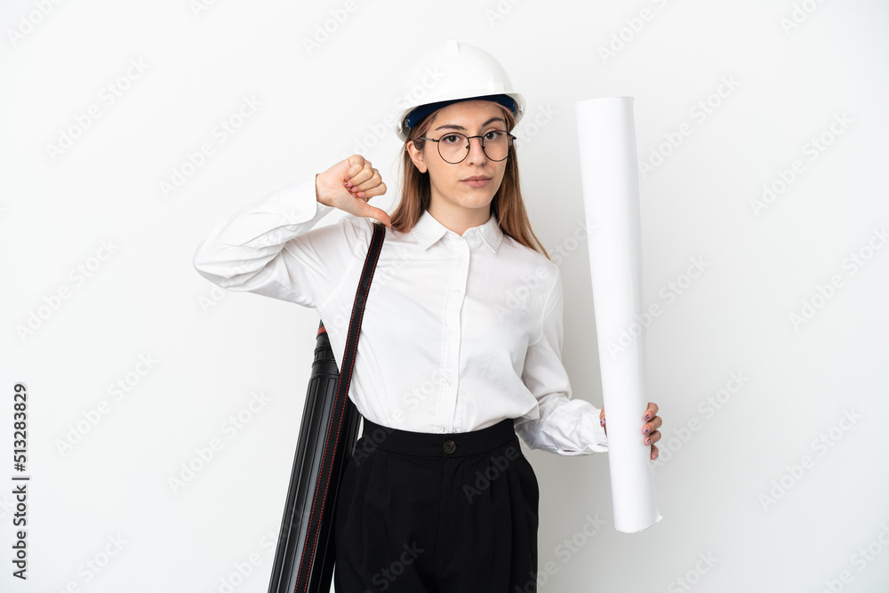 Young architect woman with helmet and holding blueprints isolated on white background showing thumb down with negative expression Young architect woman with helmet and holding blueprints isolated on white background showing thumb down with negative expression