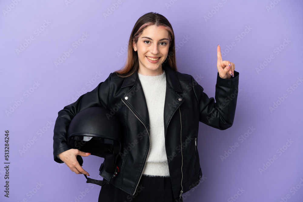Young caucasian woman holding a motorcycle helmet isolated on purple background showing and lifting a finger in sign of the best Young caucasian woman holding a motorcycle helmet isolated on purple background showing and lifting a finger in sign of the best