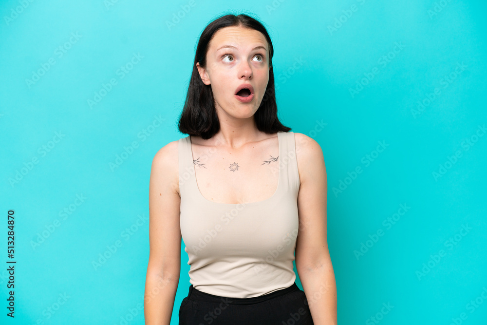 Young caucasian woman isolated on blue background looking up and with surprised expression