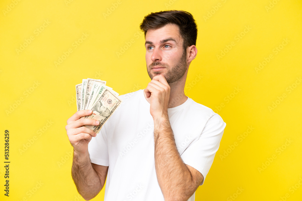 Young caucasian man taking a lot of money isolated on yellow background and looking up Young caucasian man taking a lot of money isolated on yellow background and looking up
