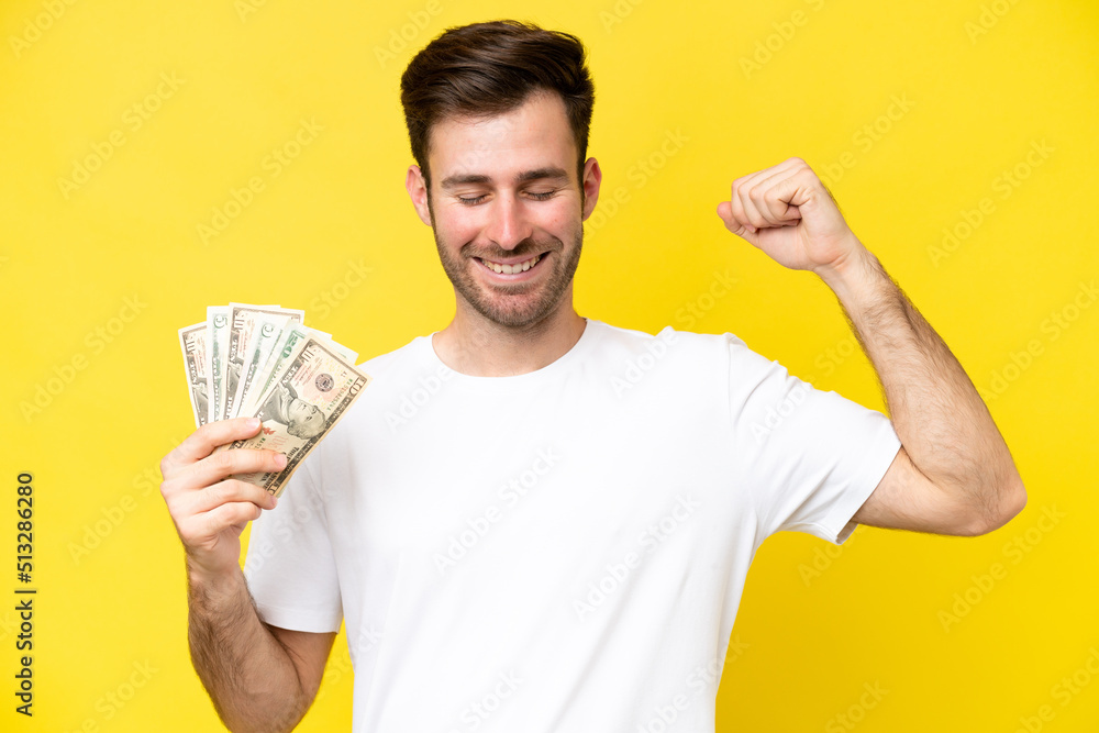 Young caucasian man taking a lot of money isolated on yellow background doing strong gesture Young caucasian man taking a lot of money isolated on yellow background doing strong gesture