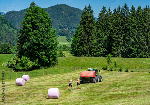Landwirtschaft im Allgäu, Bayern: Heuballen werden von zwei Männern und Großballenpresse, Maschine in Folie verpackt photo