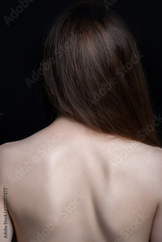 Beauty and fashion concept. Beautiful wild looking woman with naked back standing in front of camera. Model with long brown hair and smooth skin. Studio shot in black background with copy space