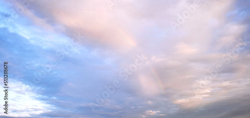 Beautiful sky and cloudscape with rainbow in light blue and rose gold colours