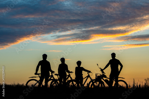 parents and kids ride bicycle at sunset. family on cycle ride in countryside. Silhouette of cyclist