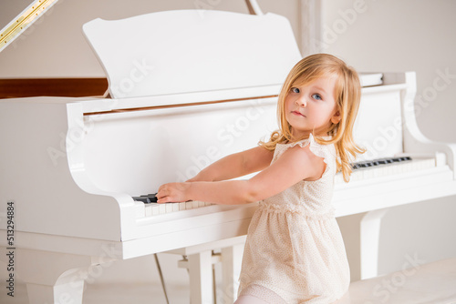A little baby plays a big white piano in a bright sunny room