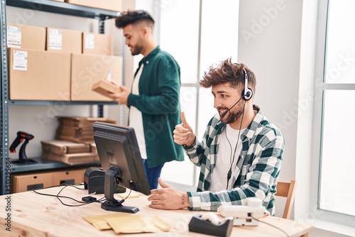 Two hispanic men working at small business ecommerce smiling happy and positive, thumb up doing excellent and approval sign