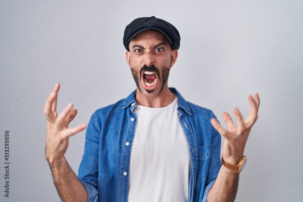 Hispanic man with beard standing over isolated background crazy and mad shouting and yelling with aggressive expression and arms raised. frustration concept. Hispanic man with beard standing over isolated background crazy and mad shouting and yelling with aggressive expression and arms raised. frustration concept.