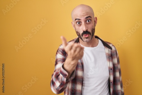 Hispanic man with beard standing over yellow background looking at the camera blowing a kiss with hand on air being lovely and sexy. love expression.