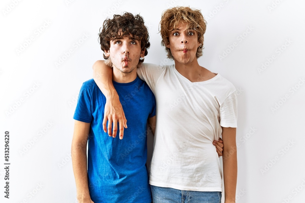 Fototapeta premium Young gay couple standing together over isolated background making fish face with lips, crazy and comical gesture. funny expression.