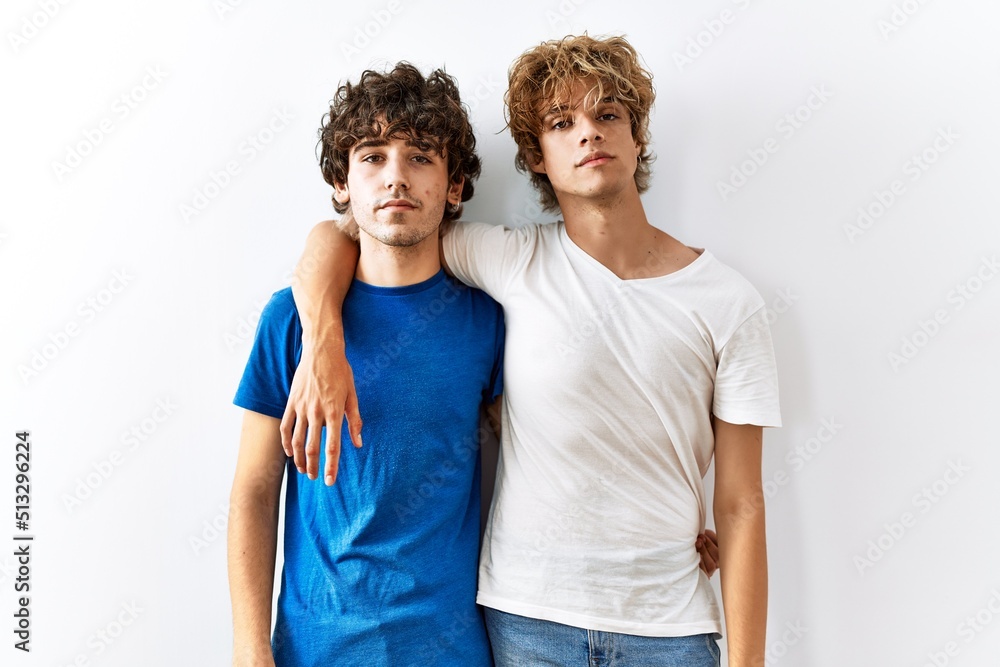 Young gay couple standing together over isolated background relaxed with serious expression on face. simple and natural looking at the camera. Young gay couple standing together over isolated background relaxed with serious expression on face. simple and natural looking at the camera.