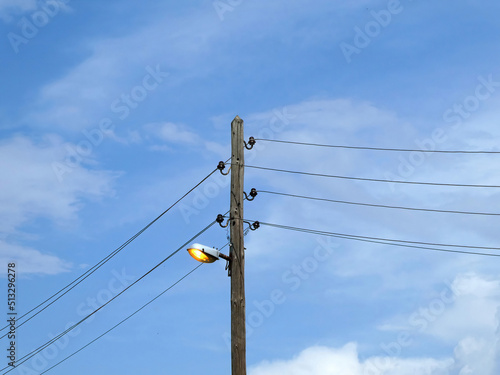 Old electricity street lamp and wires on wooden post  with blue cloudy sky  background