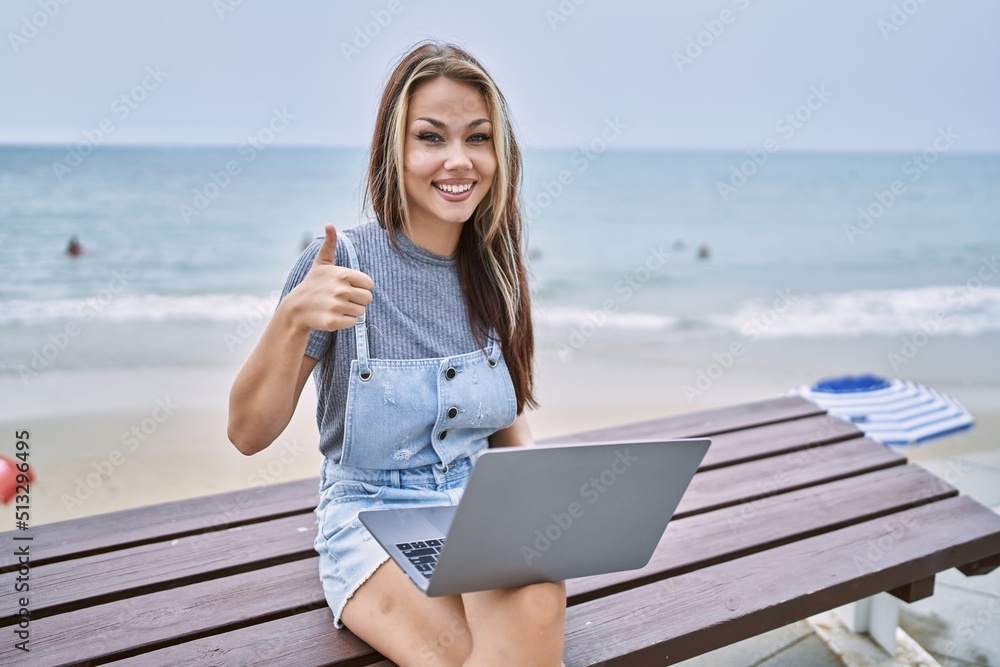 Young caucasian woman working using computer laptop outdoors smiling happy and positive, thumb up doing excellent and approval sign
