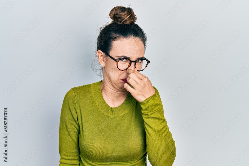 Young hispanic girl wearing casual clothes and glasses smelling something stinky and disgusting, intolerable smell, holding breath with fingers on nose. bad smell Young hispanic girl wearing casual clothes and glasses smelling something stinky and disgusting, intolerable smell, holding breath with fingers on nose. bad smell